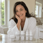 Woman in a white robe sitting at a bathroom counter with skincare products.